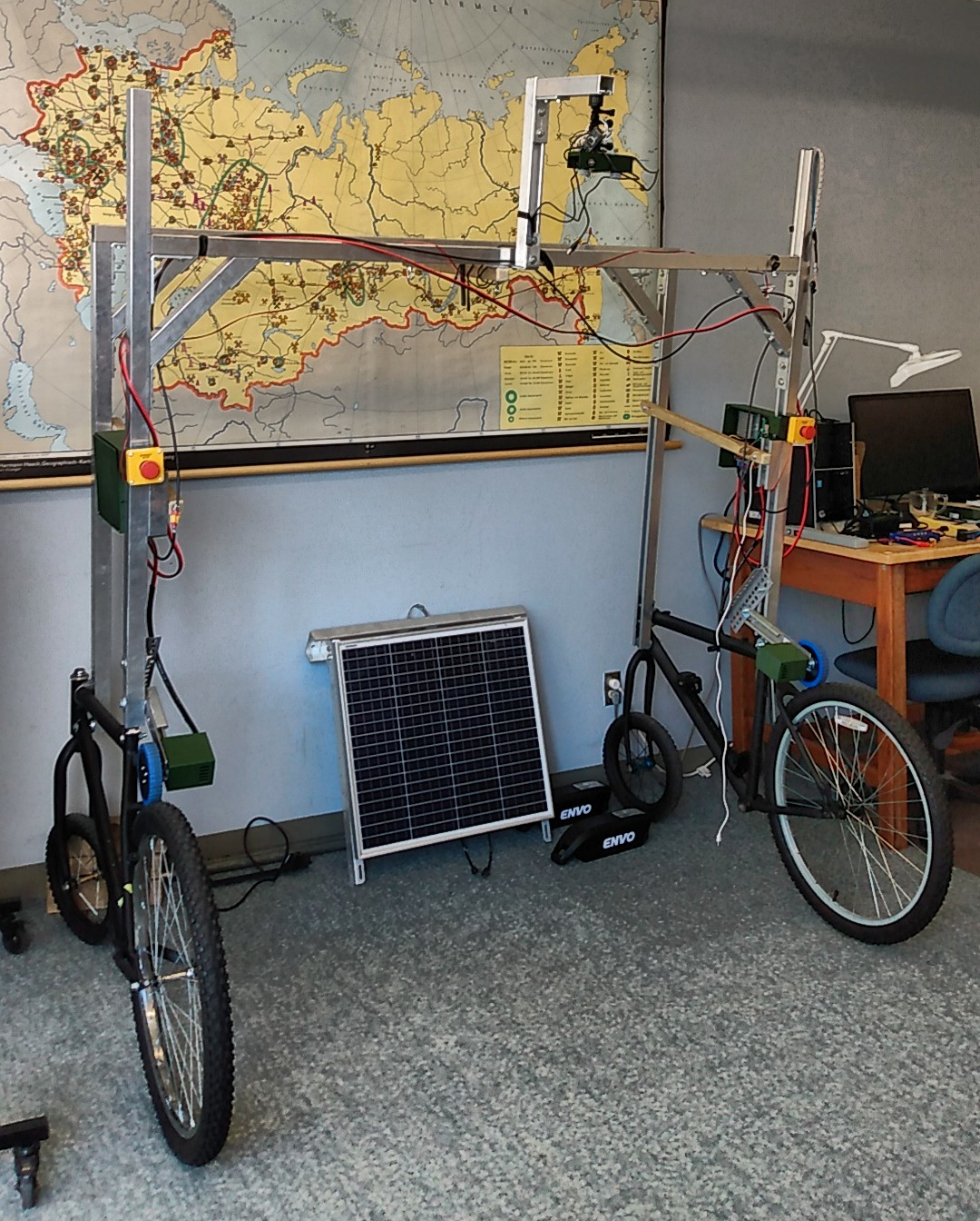 The beginning of a prototype robot constructed from 2 old bicycles and aluminum strut. A pair of Mapir cameras hang from a jib, there is a solar panel leaning against the wall which has a large wall map depicting the industrial resources of the former Soviet Union.